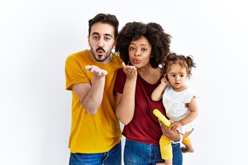 Interracial young family of black mother and hispanic father with daughter looking at the camera blowing a kiss with hand on air being lovely and sexy. love expression.