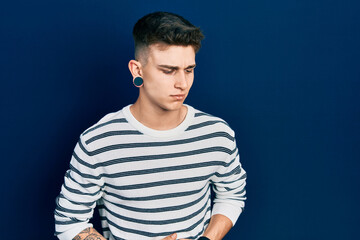 Young caucasian boy with ears dilation wearing casual striped shirt with hand on stomach because indigestion, painful illness feeling unwell. ache concept.
