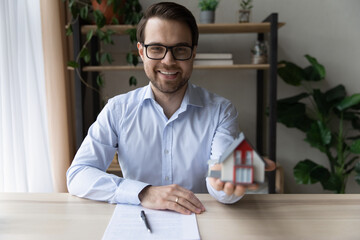 Happy male real estate or insurance agent holding house miniature, offering property for buying, apartment for rent, giving consultation, helping with mortgage. Head shot portrait