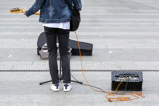 A young street musician plays an electric guitar with an amplifier on a city street.