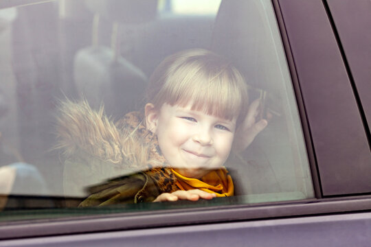 Little girl, child sitting inside the car seen from the outside. Young kid peeking from the vehicle window, portrait, closeup. Means of transport, children traveling, transportation, motion sickness
