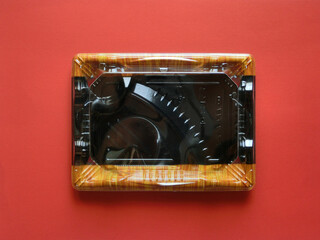 赤い紙の中央に置いたプラスチックのスーパー弁当の蓋がついた空き容器