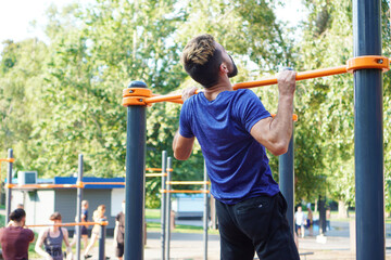 Obraz premium Athletic muscular sportsman trains on the horizontal bar in the city park