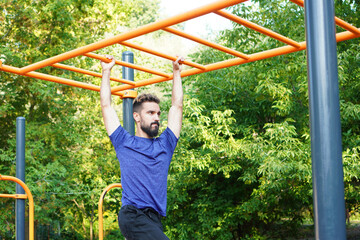Obraz premium Athletic muscular sportsman trains on the horizontal bar in the city park