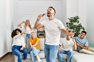 Group of young friends having party singing song using microphone at home.
