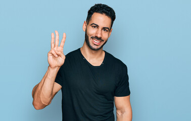 Naklejka premium Hispanic man with beard wearing casual black t shirt showing and pointing up with fingers number three while smiling confident and happy.