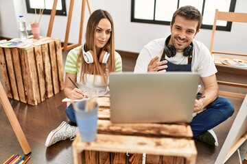 Two hispanic students having online paint class using laptop at art studio.