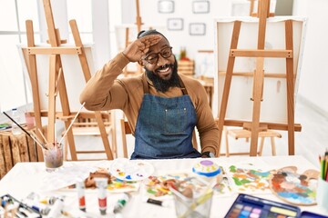 African american artist man at art studio very happy and smiling looking far away with hand over head. searching concept.