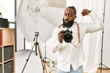 African american photographer man working at photography studio strong person showing arm muscle, confident and proud of power