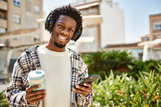 Handsome black man with afro hair wearing headphones listening to music using smartphone