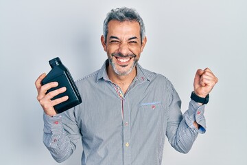 Handsome middle age man with grey hair holding motor oil bottle screaming proud, celebrating...