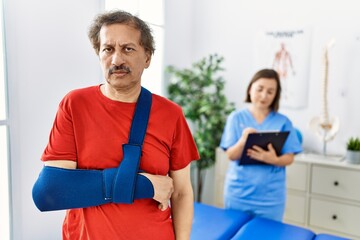 Obraz premium Southeast asian man wearing wearing arm on sling at rehabilitation clinic thinking attitude and sober expression looking self confident
