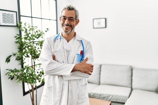 Middle age hispanic man wearing doctor uniform and stethoscope at waiting room happy face smiling with crossed arms looking at the camera. positive person.