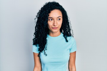 Young hispanic woman with curly hair wearing casual blue t shirt smiling looking to the side and staring away thinking.
