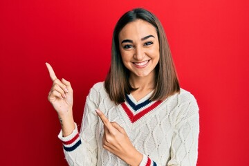 Young brunette girl wearing casual student sweater smiling and looking at the camera pointing with two hands and fingers to the side.