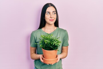 Beautiful woman with blue eyes holding green plant pot smiling looking to the side and staring away thinking.