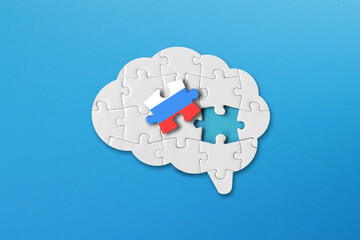 Russian learning concept, white jigsaw puzzle pieces with russian flag a human brain shape on blue background