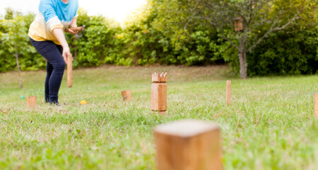 Frau spielt Wikingerschach (Kubb) im Garten. Woman plays viking chess in the garden. Wooden Kubb...