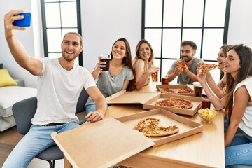 Group of young people smiling happy eating italian pizza and make selfie by the smartphone at home