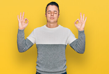 Handsome young man wearing casual winter sweater relax and smiling with eyes closed doing meditation gesture with fingers. yoga concept.