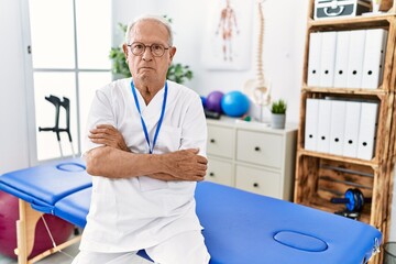 Senior physiotherapy man working at pain recovery clinic skeptic and nervous, disapproving expression on face with crossed arms. negative person.