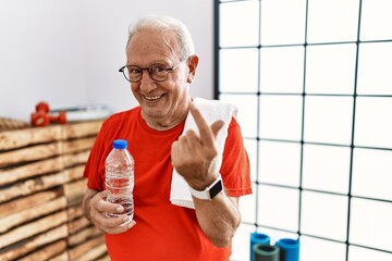 Senior man wearing sportswear and towel at the gym beckoning come here gesture with hand inviting welcoming happy and smiling