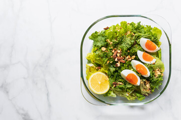 Green salad and kale with boiled egg, almond, nuts and lemon on white marble table; top view and copy space.