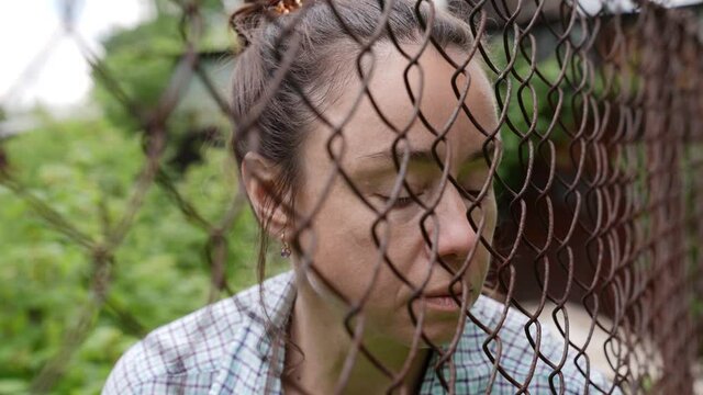 close-up portrait of a sad adult female prisoner behind a metal fence in places of detention