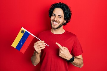 Handsome hispanic man holding venezuelan flag smiling happy pointing with hand and finger