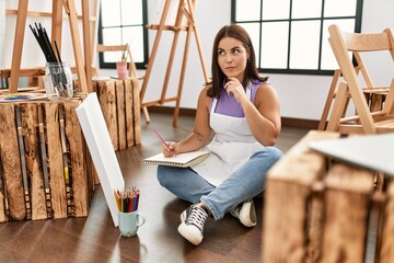 Young beautiful hispanic woman at art studio serious face thinking about question with hand on chin, thoughtful about confusing idea