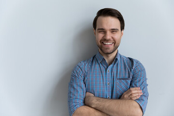 Portrait of happy millennial guy in casual shirt standing isolated by white background with arms...