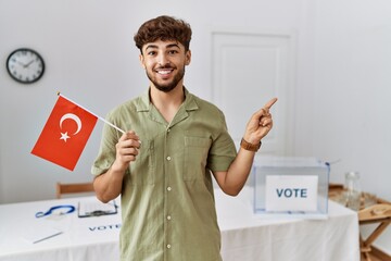 Young arab man at political campaign election holding turkey flag smiling happy pointing with hand...