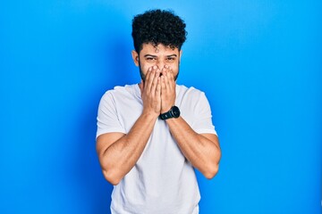 Young arab man with beard wearing casual white t shirt laughing and embarrassed giggle covering...