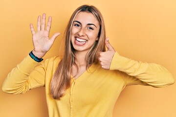 Beautiful hispanic woman wearing casual yellow sweater showing and pointing up with fingers number six while smiling confident and happy.