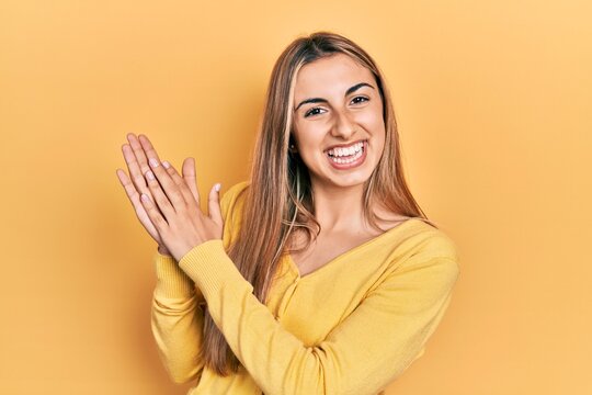 Beautiful hispanic woman wearing casual yellow sweater clapping and applauding happy and joyful, smiling proud hands together