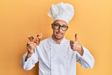 Bald man with beard wearing professional cook apron holding italian pizza smiling happy and positive, thumb up doing excellent and approval sign