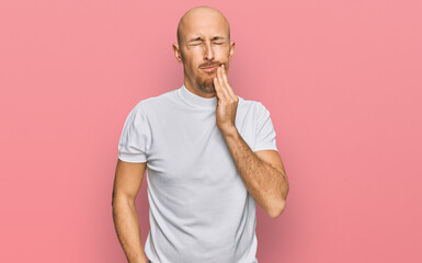 Bald man with beard wearing casual white t shirt touching mouth with hand with painful expression because of toothache or dental illness on teeth. dentist