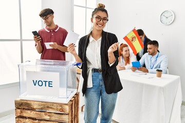 Young spanish voter woman smiling happy holding spain flag at vote center.