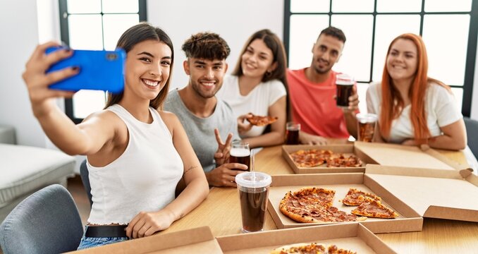 Group of young people smiling happy eating italian pizza make selfie by the smartphone at home