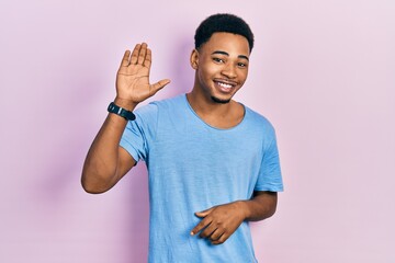 Young african american man wearing casual blue t shirt waiving saying hello happy and smiling, friendly welcome gesture