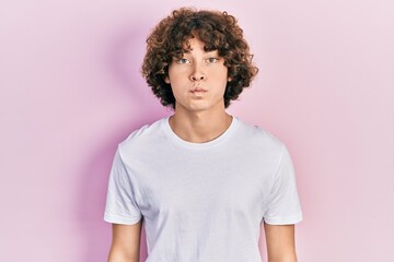 Handsome young man wearing casual white t shirt puffing cheeks with funny face. mouth inflated with...