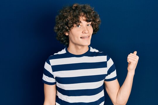 Handsome young man wearing casual striped t shirt smiling with happy face looking and pointing to the side with thumb up.