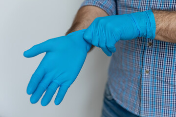 Obraz premium Hands of man wearing blue protective rubber gloves, staying safe from bacteria and virus, caring of hygiene, protecting hands from infection, preventing coronavirus spread. Close up, cropped shot