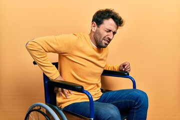 Handsome man with beard sitting on wheelchair suffering of backache, touching back with hand, muscular pain