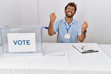 Young handsome man at political election sitting by ballot very happy and excited doing winner...