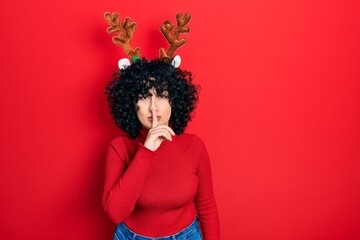 Young middle east woman wearing cute christmas reindeer horns asking to be quiet with finger on lips. silence and secret concept.