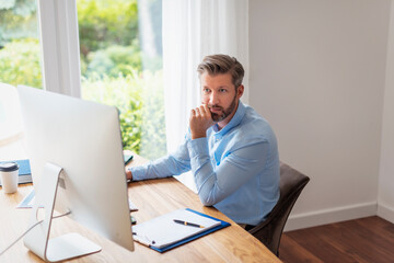 Businessman working on computer while sitting at desk at home and thinking