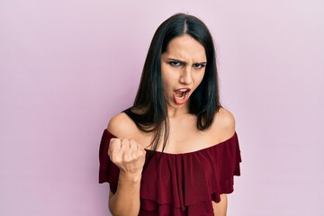Young hispanic woman wearing casual clothes angry and mad raising fist frustrated and furious while...