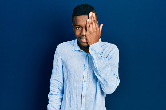 Young african american man wearing casual clothes covering one eye with hand, confident smile on face and surprise emotion.