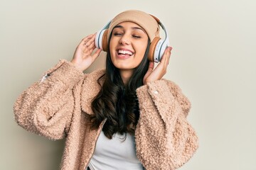 Young hispanic woman listening to music using headphones smiling and laughing hard out loud because funny crazy joke.